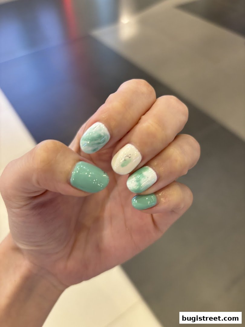 A close-up shot of a hand with beautifully manicured nails featuring a mint green and white marble design.