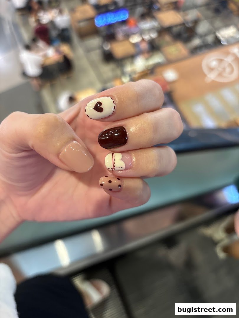 A close-up of a hand with beautifully designed nails featuring hearts and polka dots.