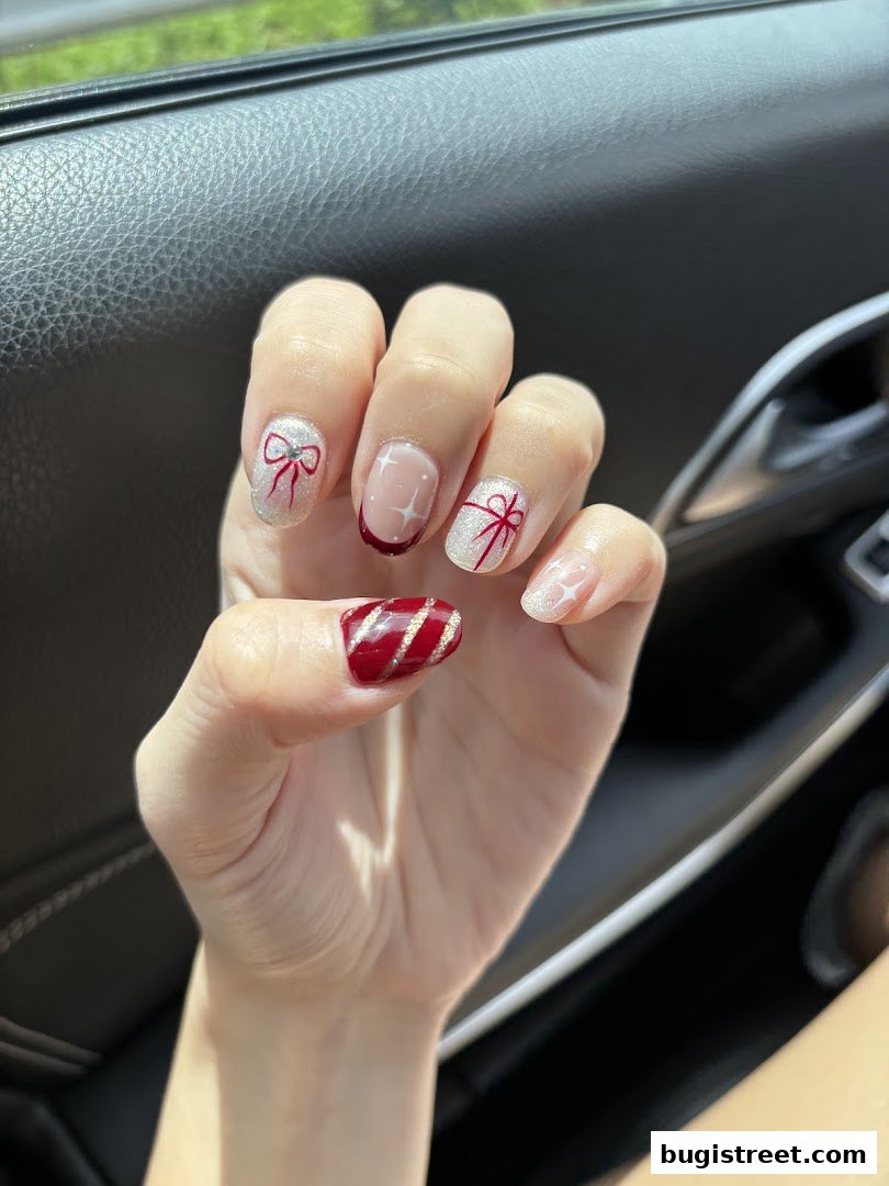 A close-up of a hand with festive red and white nail art featuring bows and glitter.