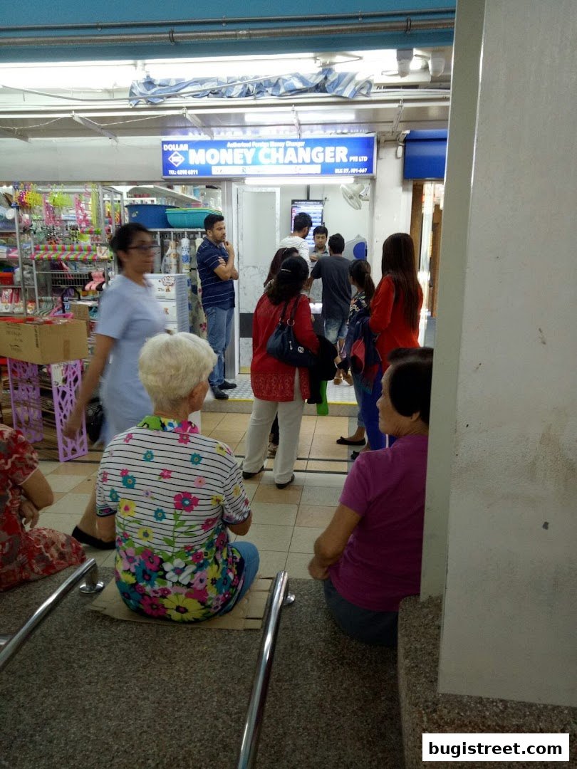 People waiting outside a Dollar Money Changer shop with a sign and merchandise visible.