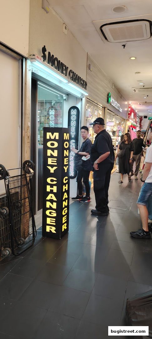 A money changer shop with bright neon signs and people standing outside.