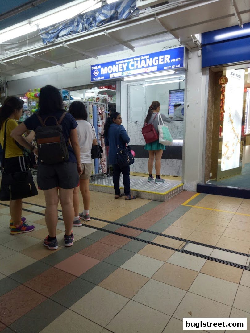 People queuing at a money changer shop with a prominent sign.