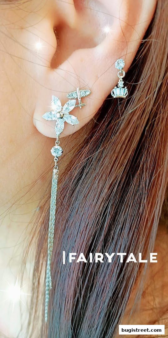 Close-up of a person wearing delicate, sparkling earrings with floral and crown motifs.