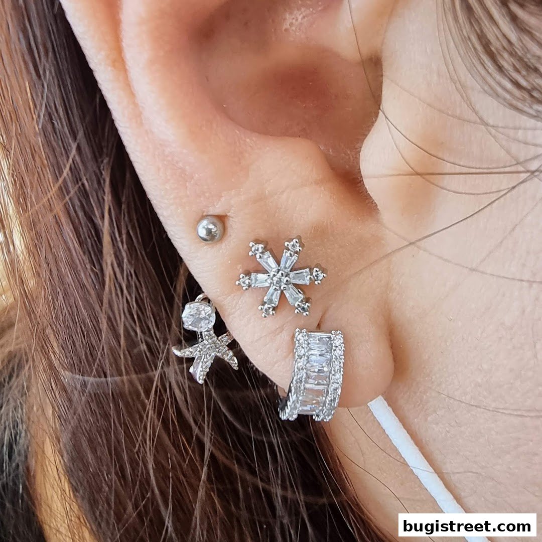 Close-up of a person's ear adorned with multiple sparkling silver earrings.