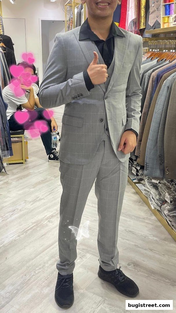 A person in a grey checkered suit gives a thumbs up in a clothing store.