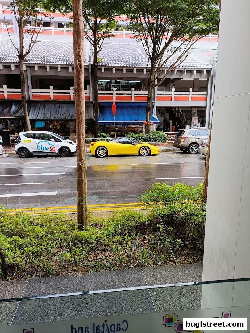 A yellow sports car parked on a wet street in front of shops.