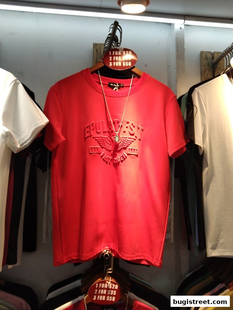 A red t-shirt with embossed text and a necklace is displayed on a hanger.