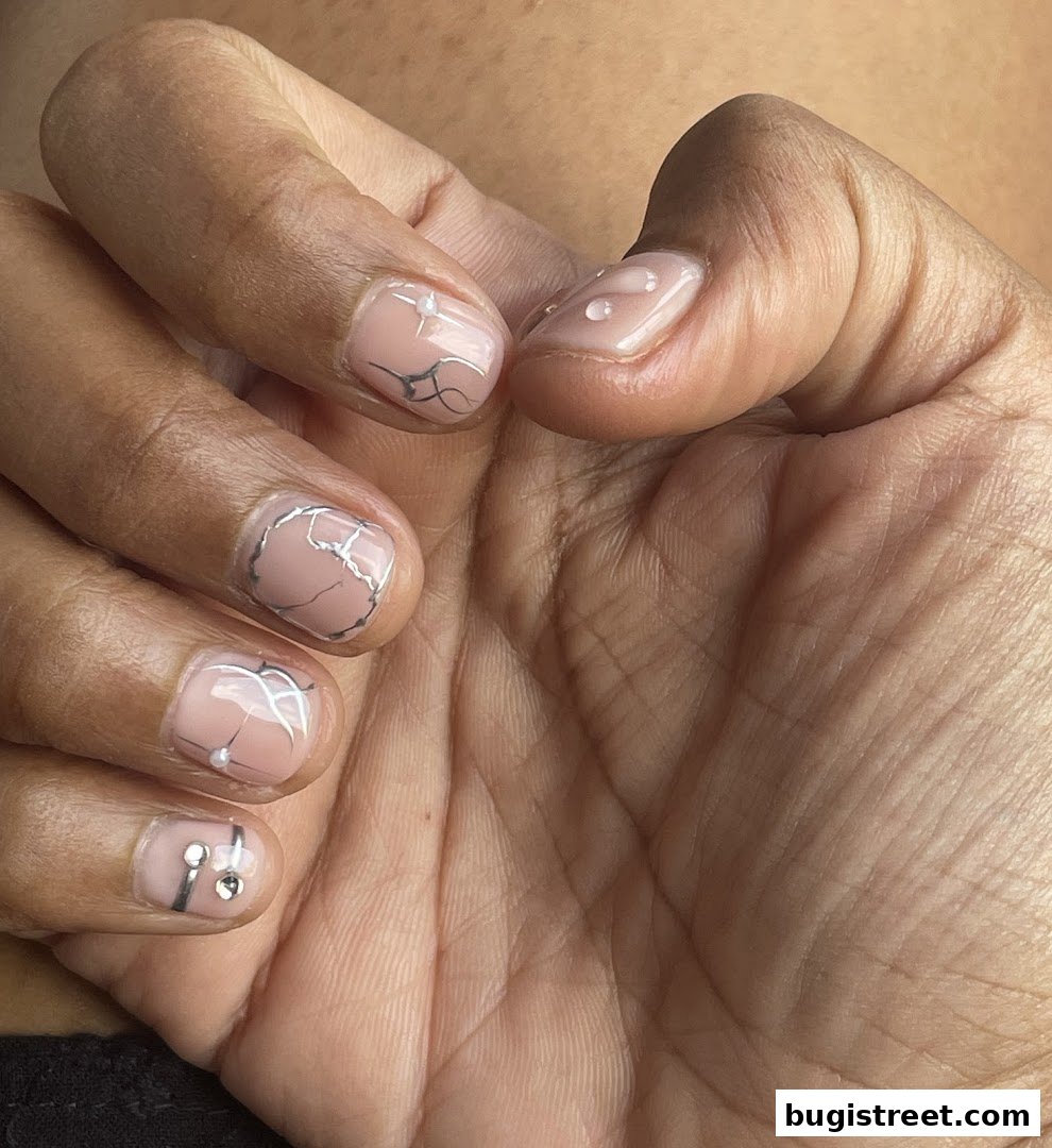 Close-up of a hand with elegant, minimalist nail art featuring silver lines and small embellishments.