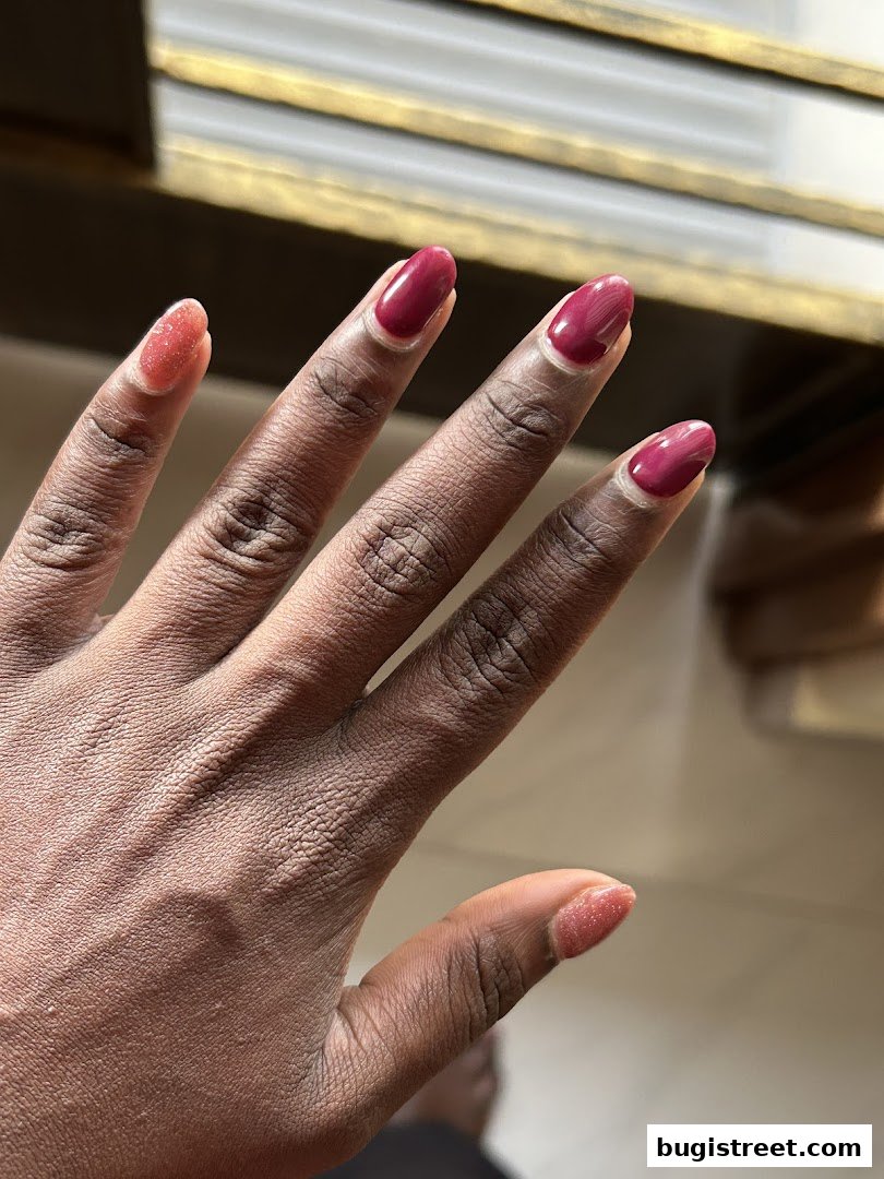 A close-up of a hand with beautifully manicured nails in a deep red shade and glitter accents.
