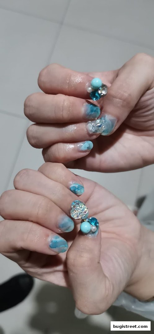 Close-up of hands with intricate blue and white marbled nail art, adorned with gems and pearls.