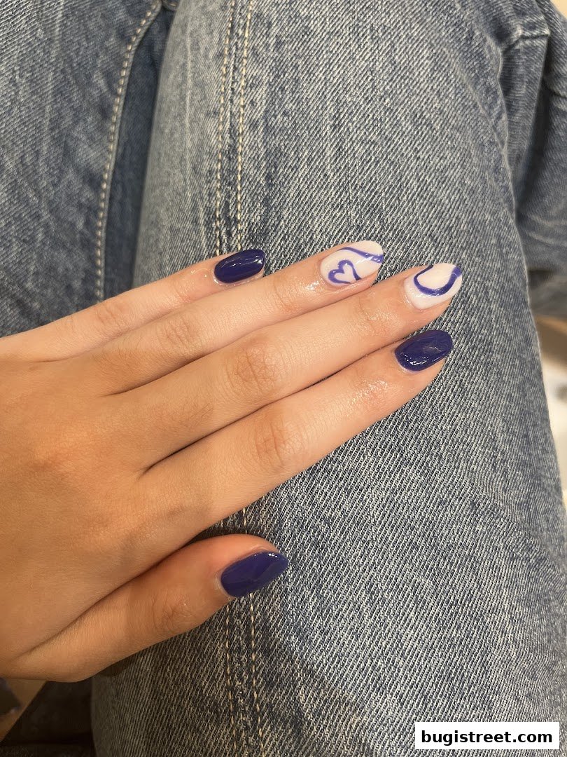 A close-up of a hand with dark blue and white nails featuring purple heart designs.