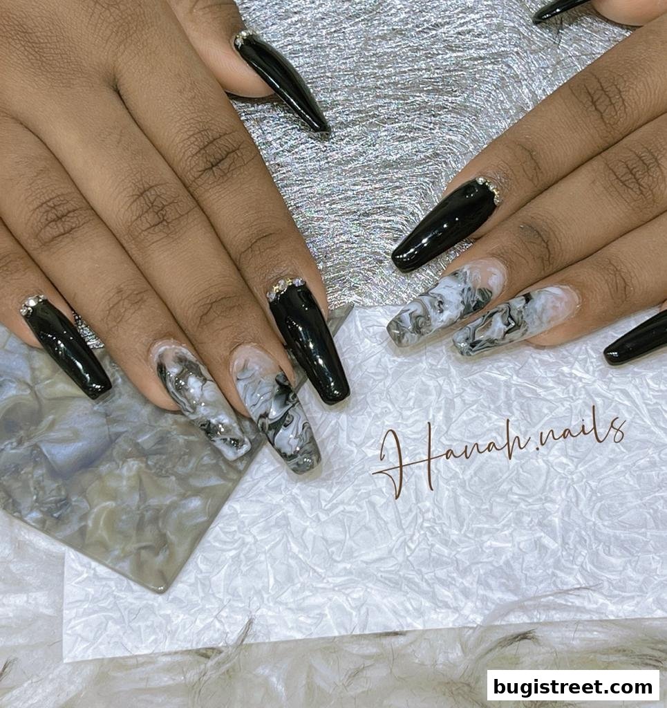 Close-up of hands with black and marble-patterned coffin nails adorned with rhinestones.