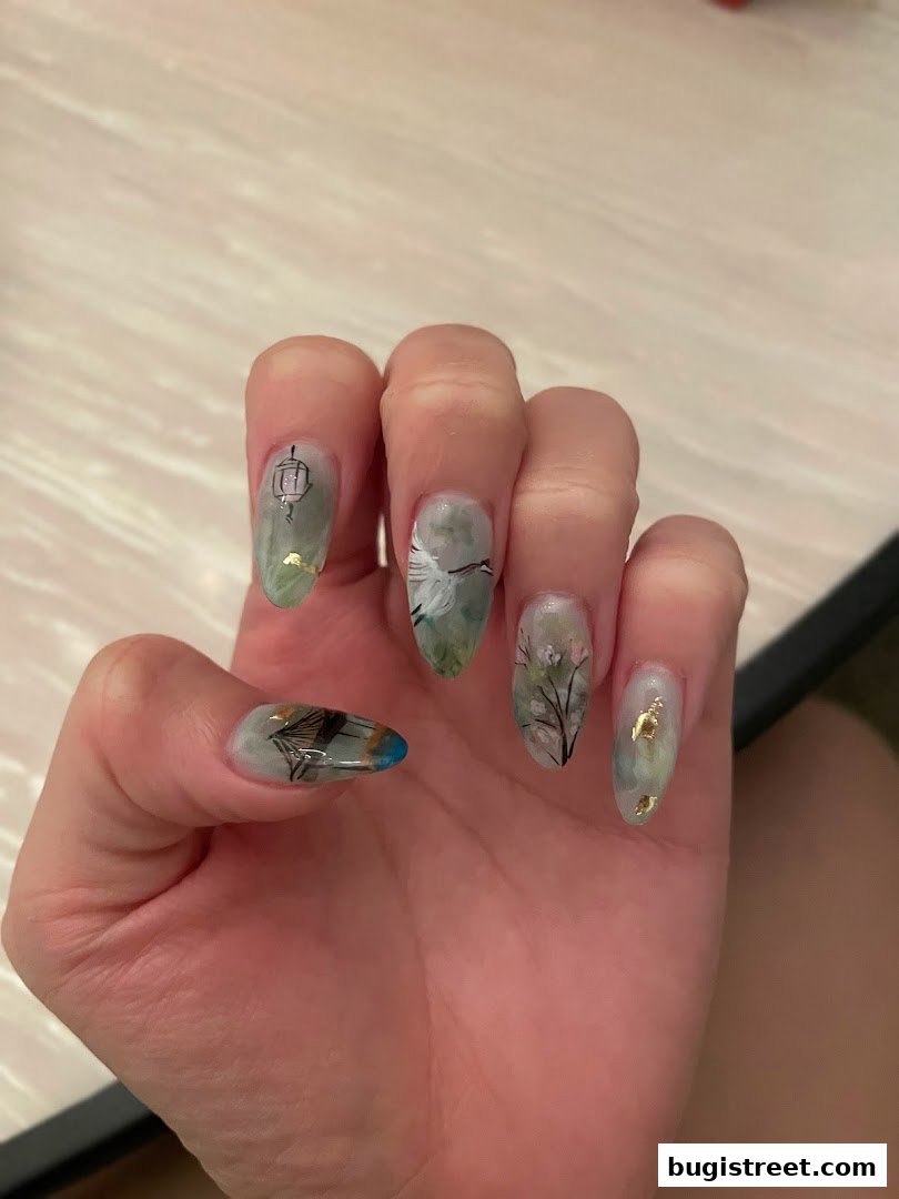 A hand with intricately designed nails featuring nature-inspired artwork and gold leaf accents.