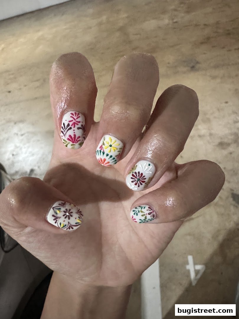 A hand with beautifully decorated nails featuring intricate floral patterns in vibrant colors.