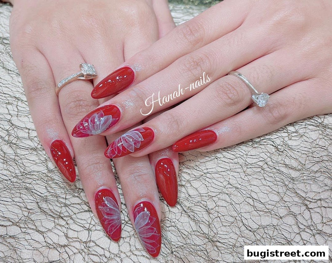 Close-up of hands with glossy red stiletto nails featuring delicate white floral designs.
