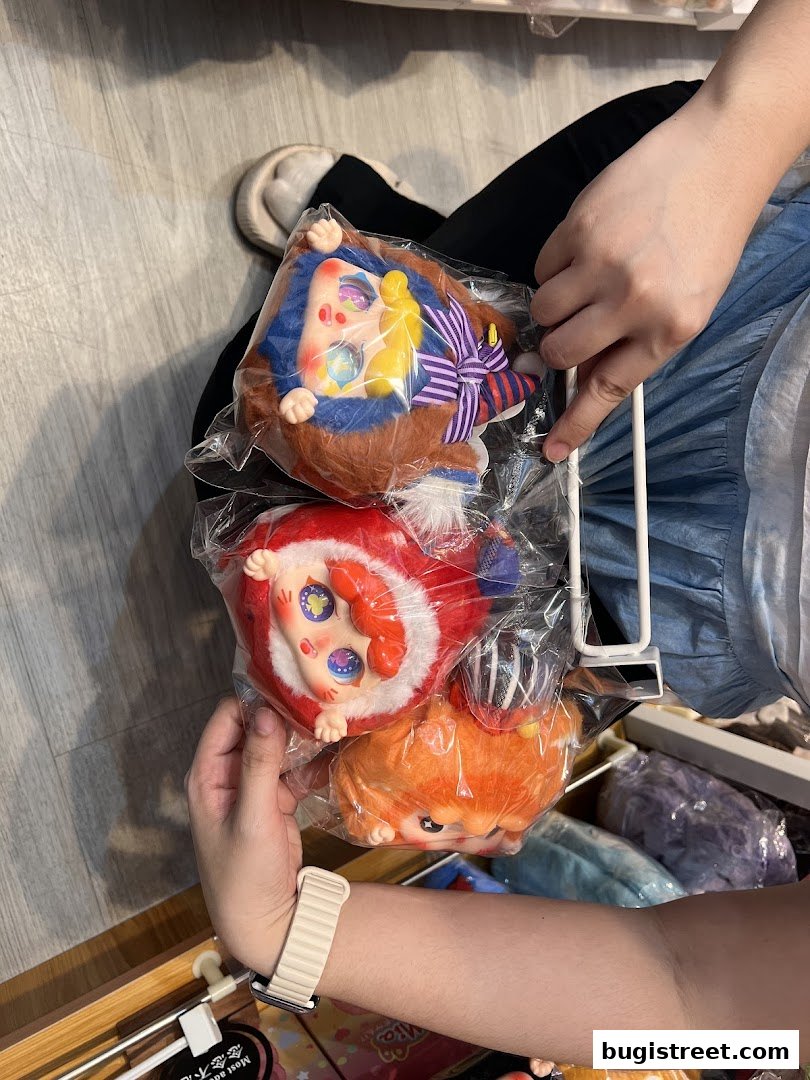 Hands holding three plush toys with large eyes and colorful outfits.