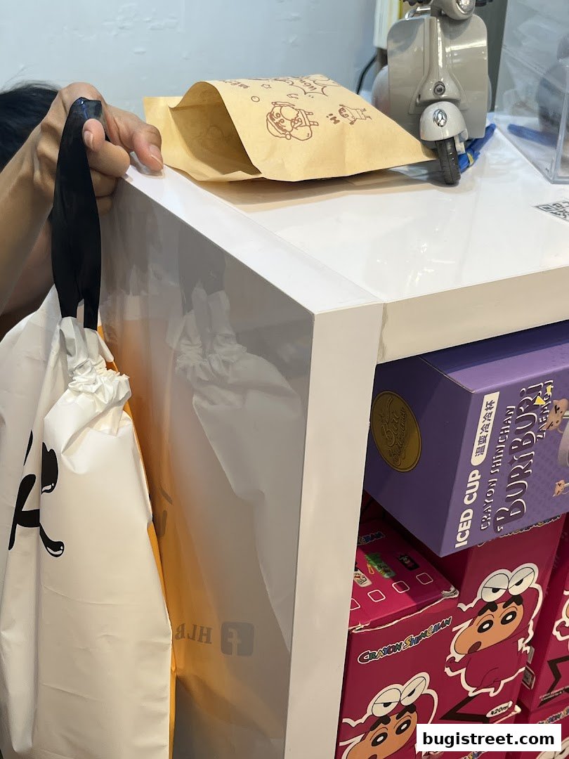 A person holds a shopping bag next to a display of Crayon Shin-chan merchandise.