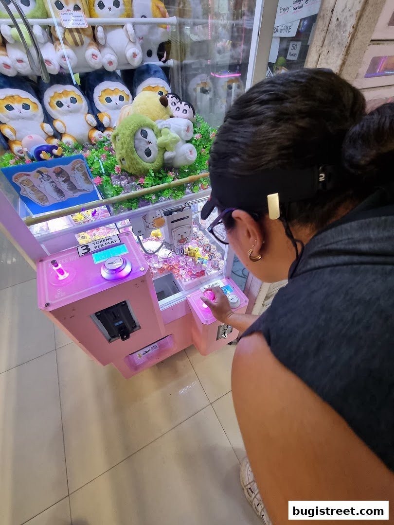 A person plays a pink claw machine filled with plush toys.