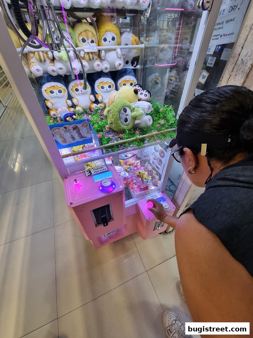A person plays a pink claw machine filled with plush toys and prizes.