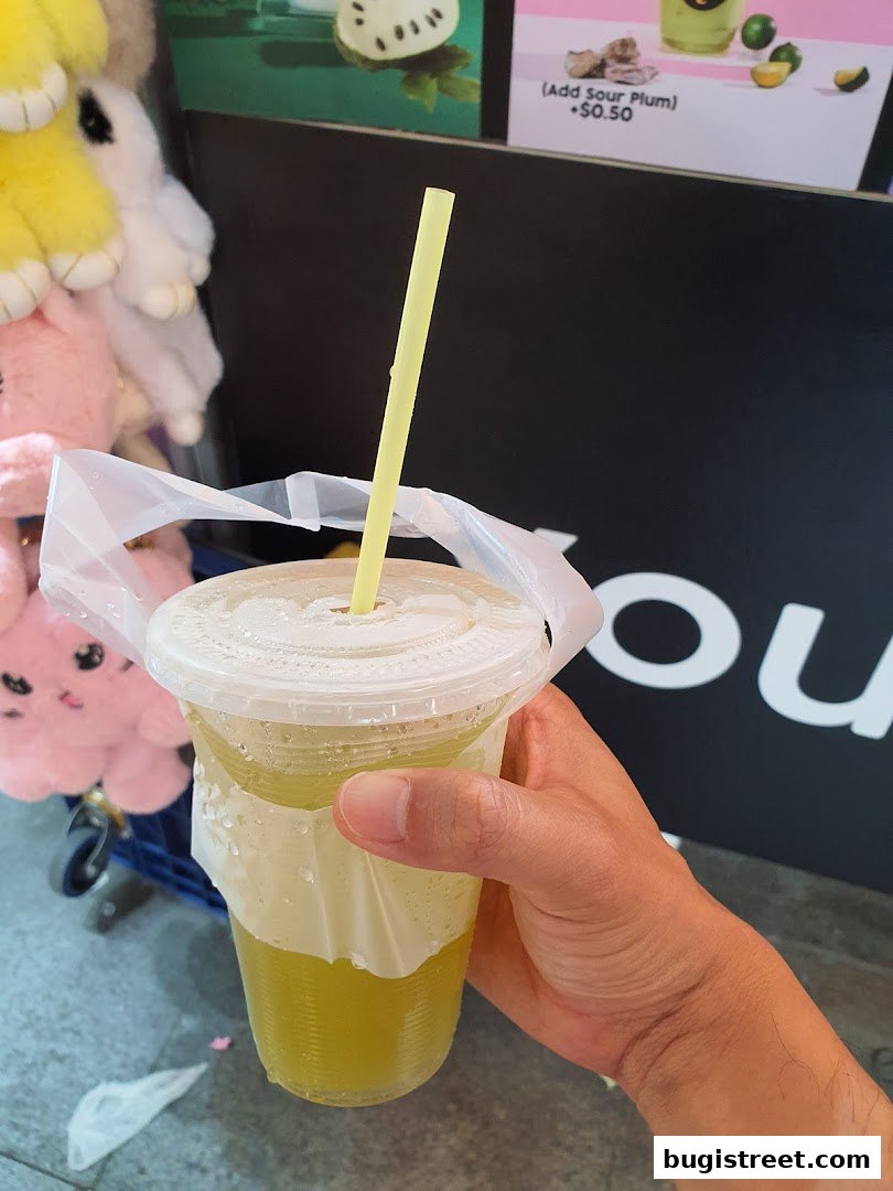 A hand holds a refreshing cup of green juice with a yellow straw, ready to be enjoyed.