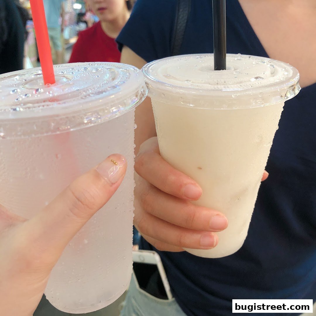 Two people holding refreshing, frosted cups of juice with straws.