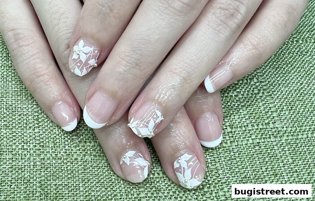 Close-up of hands with elegant white floral nail art and French tips.