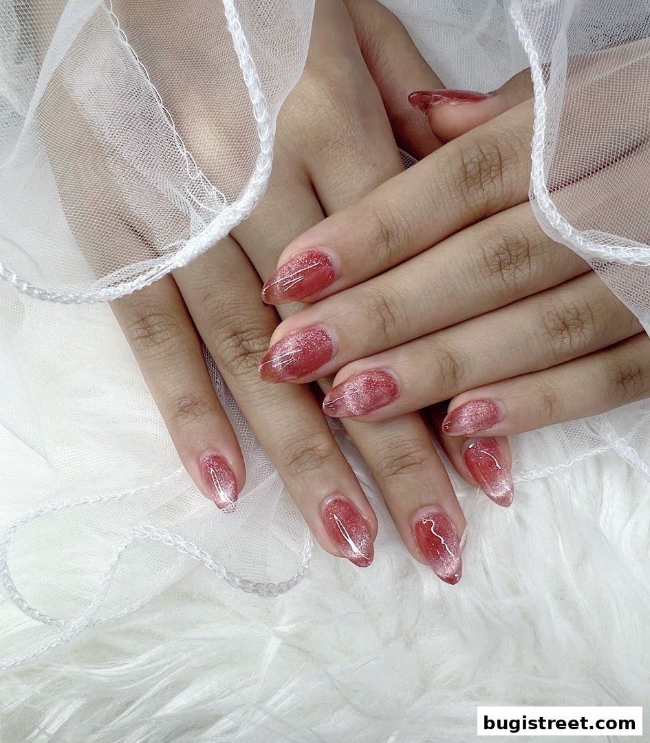 Close-up of hands with beautifully manicured, sparkly red almond-shaped nails.