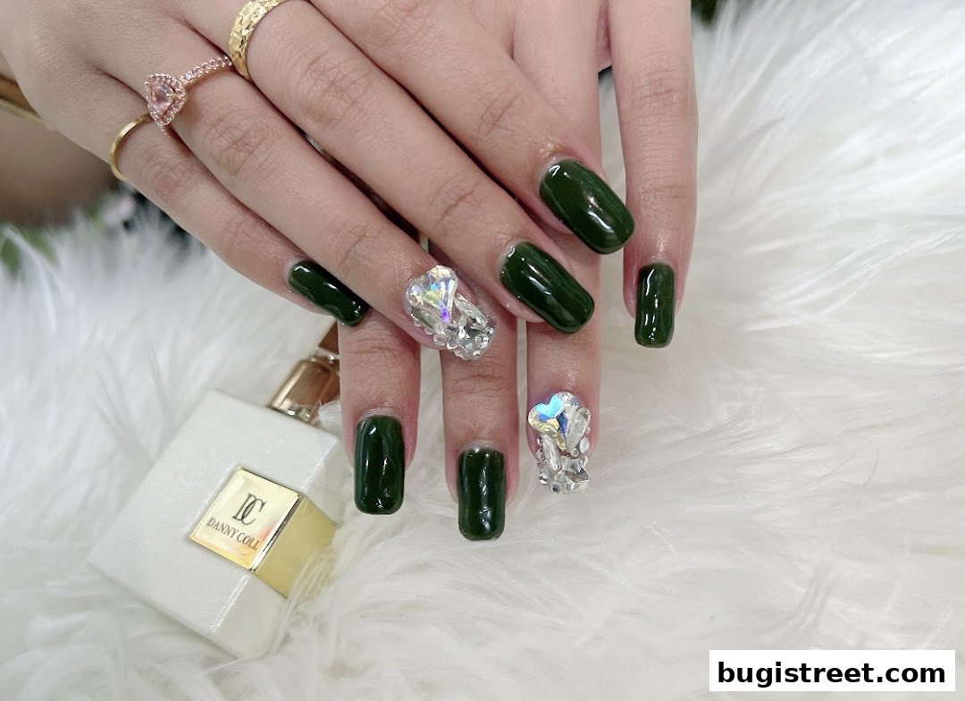Close-up of hands with dark green gel nails adorned with sparkling rhinestones.
