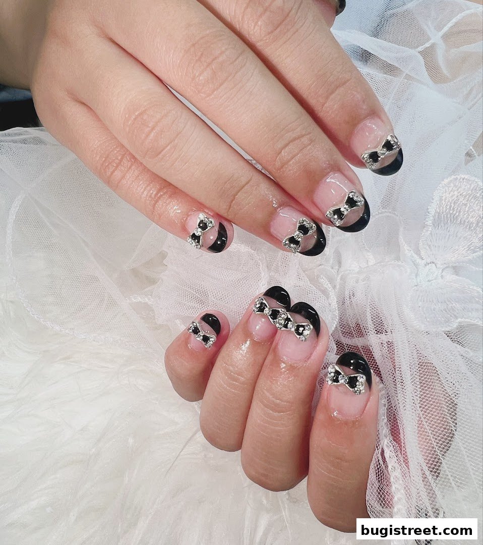 Close-up of hands with elegant black and clear French tip nails adorned with sparkling bow charms.