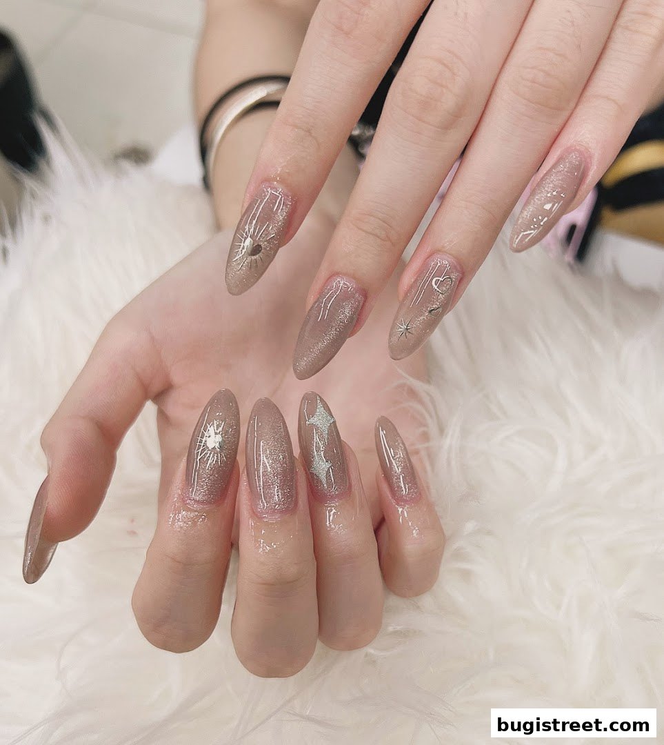 Close-up of a person's hands with beautifully designed, long, almond-shaped nails featuring a nude base and celestial-themed embellishments.