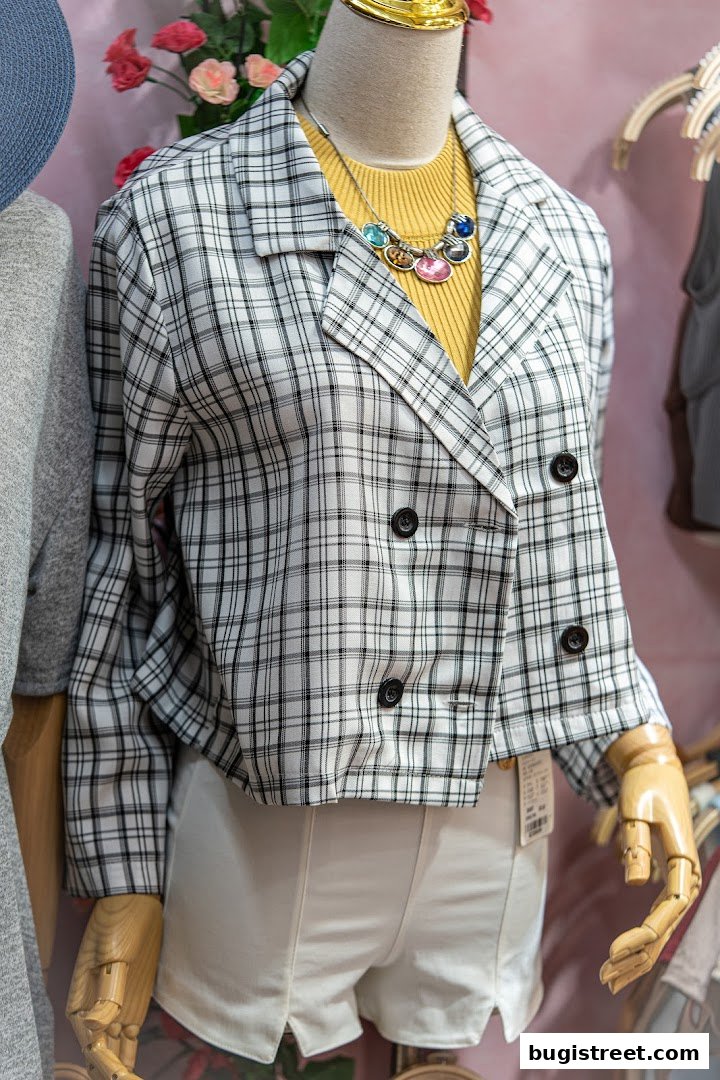 Mannequin wearing a plaid jacket, yellow top, and white shorts with a colorful necklace.