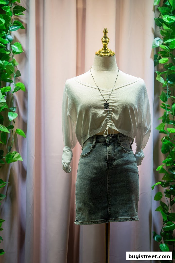 Mannequin wearing a white ruched top and denim skirt, displayed with greenery.