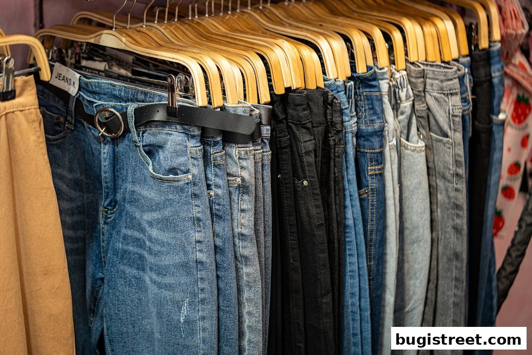 A rack of various denim jeans and a tan pair of pants hanging on wooden hangers.