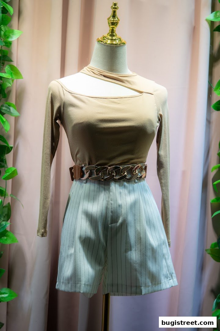 A mannequin displays a stylish outfit with a beige cutout top and pinstripe shorts.