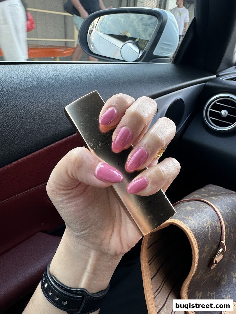 A hand with perfectly manicured pink nails holds a golden object inside a car.