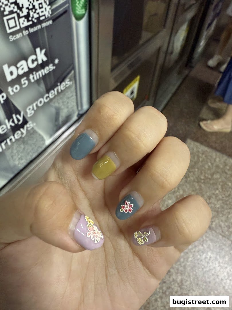 A close-up of a hand with beautifully decorated nails featuring floral designs and pastel colors.