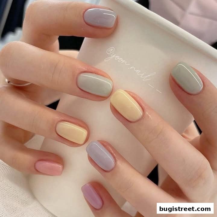 Close-up of hands with pastel-colored nails holding a white cup.