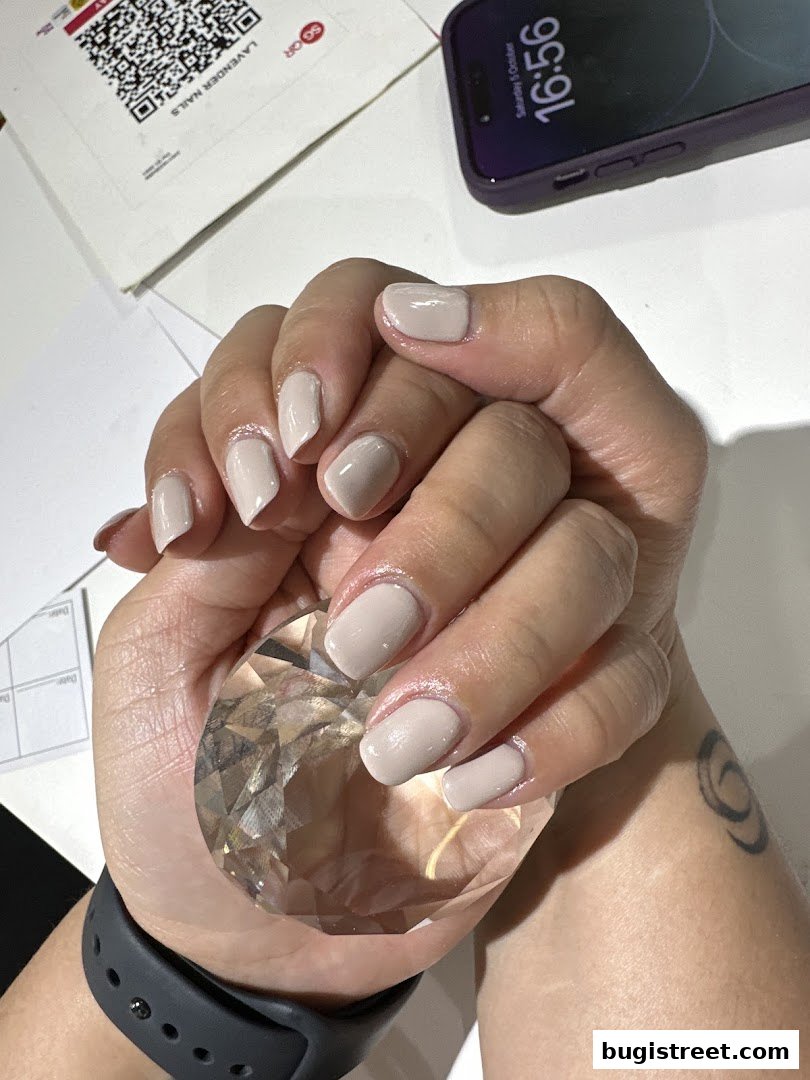 A close-up of hands with neatly painted neutral-colored nails holding a crystal.