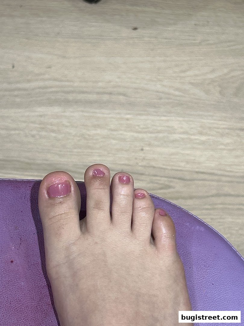 A close-up of a foot with freshly painted pink toenails resting on a purple surface.