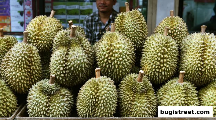 A display of fresh durian fruits with a vendor in the background.