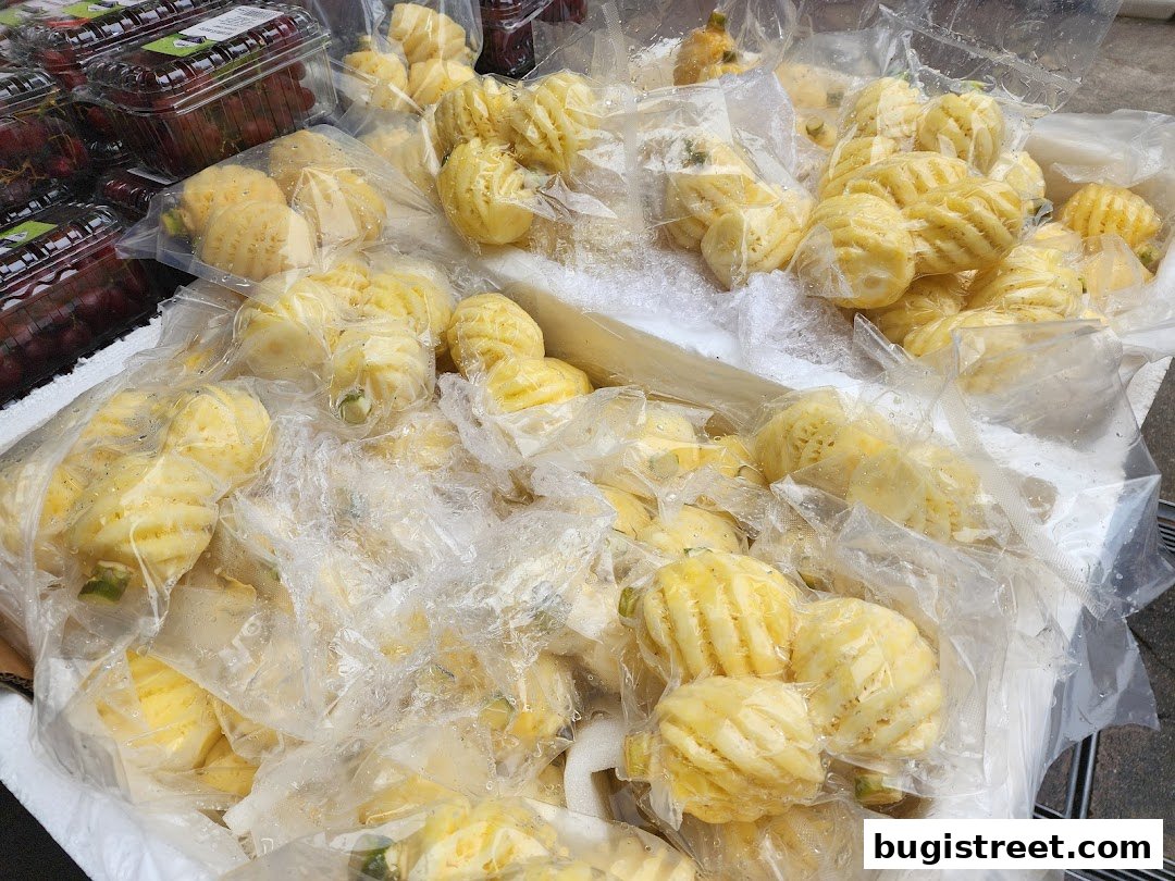 A close-up view of pre-peeled pineapples packaged in plastic bags, with grapes in the background.