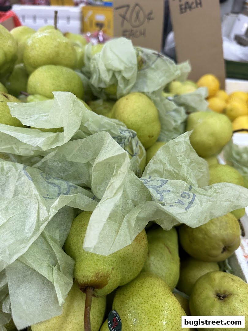 A close-up shot of fresh pears, some wrapped in light green paper, with a price sign in the background.