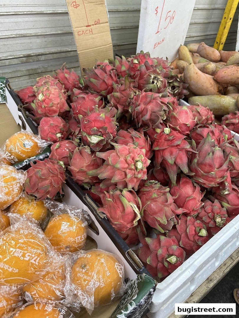 A close-up view of fresh dragon fruits and oranges displayed in boxes at a fruit stall.