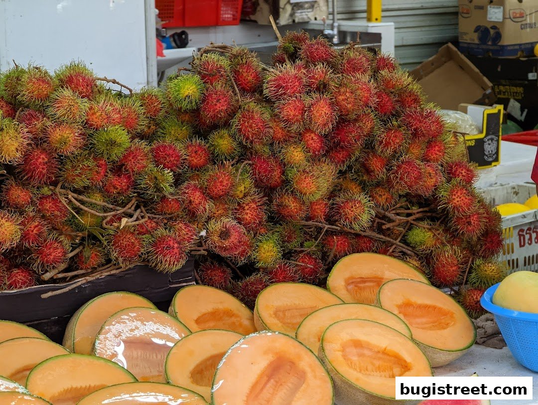 A vibrant display of fresh rambutan fruits and sliced cantaloupe at a fruit stall.