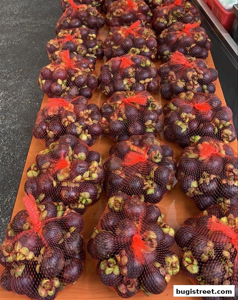 Bags of fresh mangosteen fruits are neatly arranged on a wooden surface.