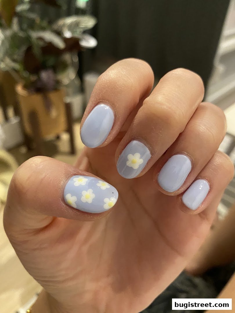 A close-up of a hand with light blue nails adorned with delicate white flower designs.