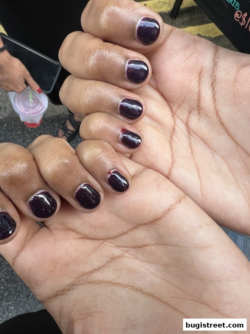 Close-up of hands with dark purple gel manicured nails, some showing minor chips.