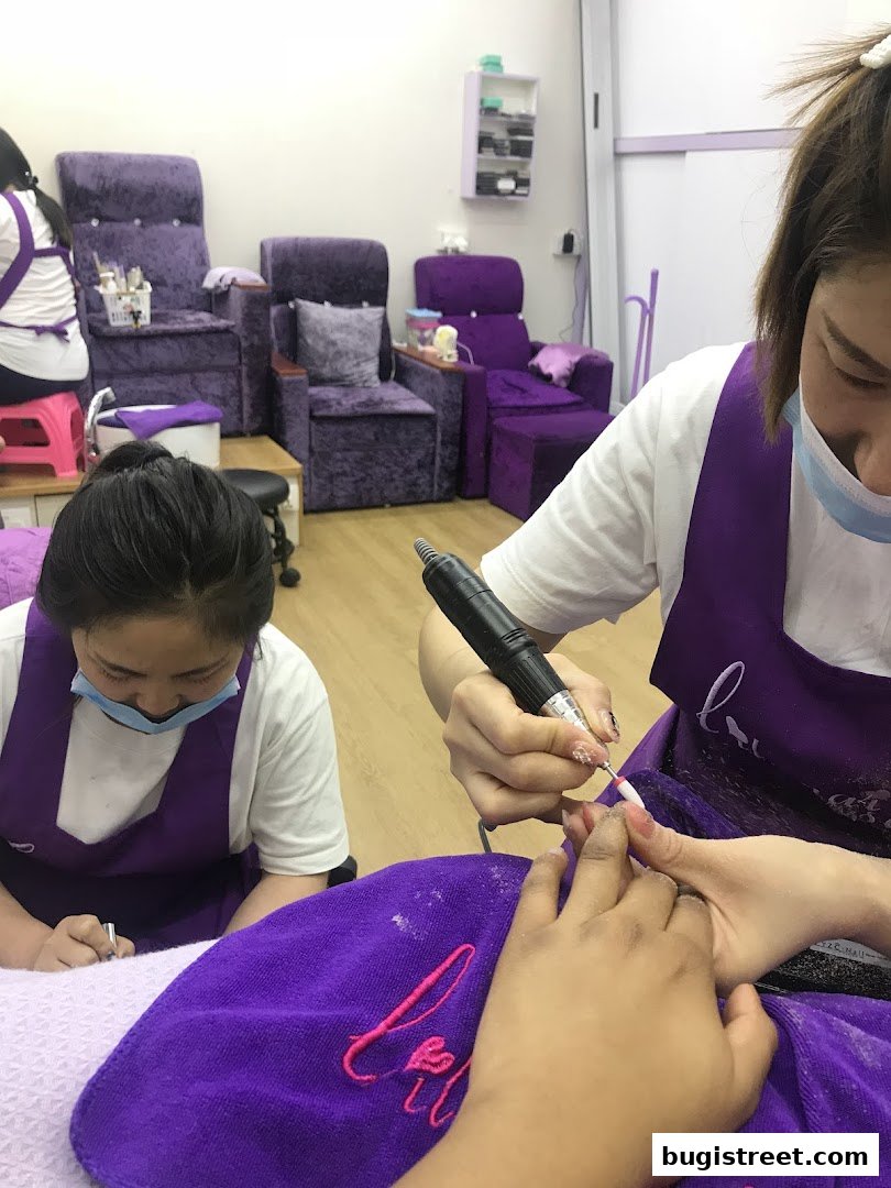 Nail technicians working on clients' nails in a salon with purple chairs.