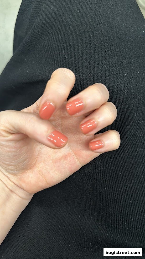 A close-up of a hand with perfectly manicured nails painted in a vibrant coral shade.