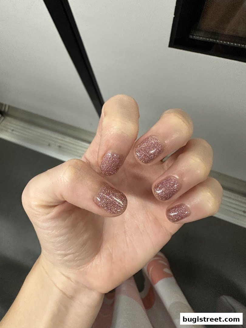 A close-up shot of a hand with short, glittery rose gold nails.